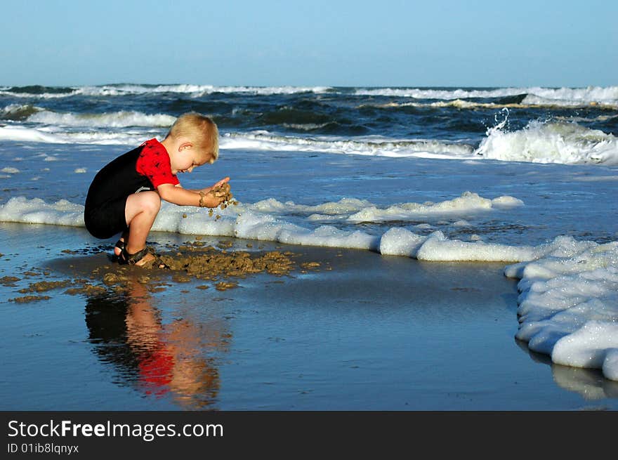 Boy playing in sand at water's edge. Boy playing in sand at water's edge