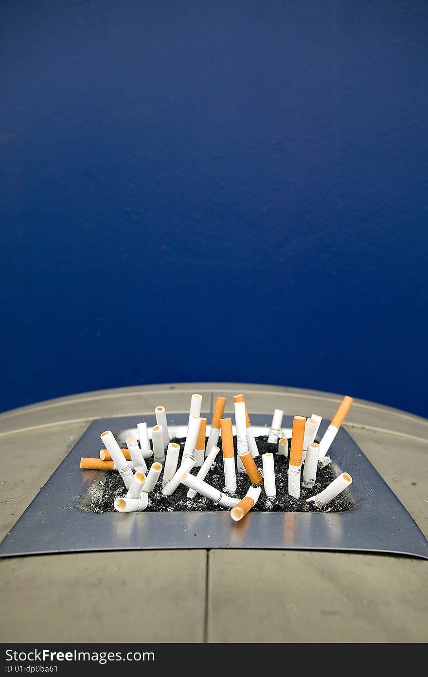 Ashtray in the lid of a trashcan outside a large department store against a blue wall. Ashtray in the lid of a trashcan outside a large department store against a blue wall.