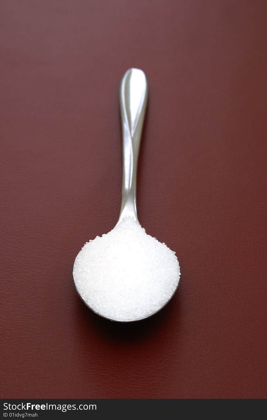 A teaspoon of sugar on red background.