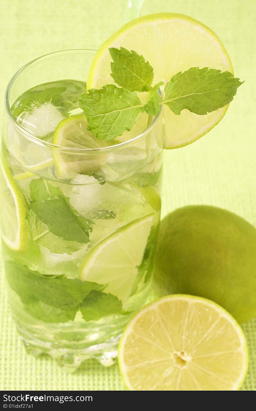 Mojito cocktail with lime, mint leaves and ice on green background. Mojito cocktail with lime, mint leaves and ice on green background