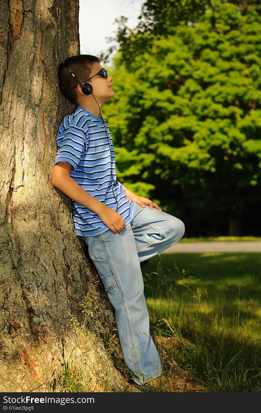 Boy listens to music having leant against a tree