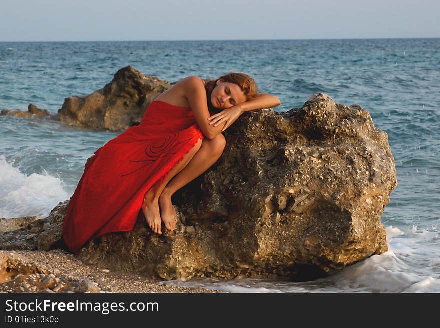 Young girl in orange dress lying on a rock on the sea shore, eyes closed. Young girl in orange dress lying on a rock on the sea shore, eyes closed