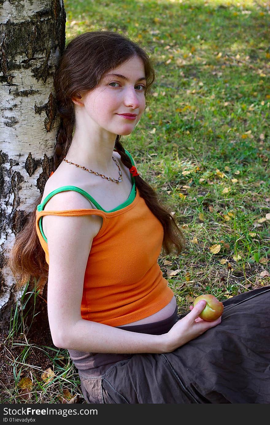 Pregnant girl sitting with an apple under a tree