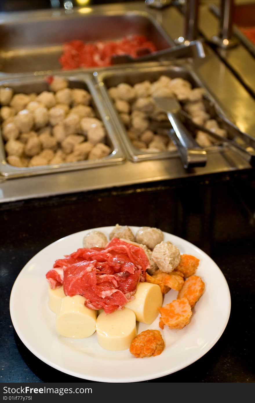 Raw food on a white plate in front of buffet table, ready to be boiled. Raw food on a white plate in front of buffet table, ready to be boiled