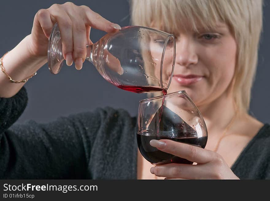 The blonde pours from a glass in a glass red wine. The blonde pours from a glass in a glass red wine.