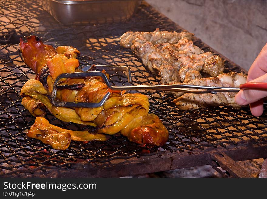 Pork fillet and chicken kebabs being grilled on an open fire and being turned by hand with tongs. Pork fillet and chicken kebabs being grilled on an open fire and being turned by hand with tongs