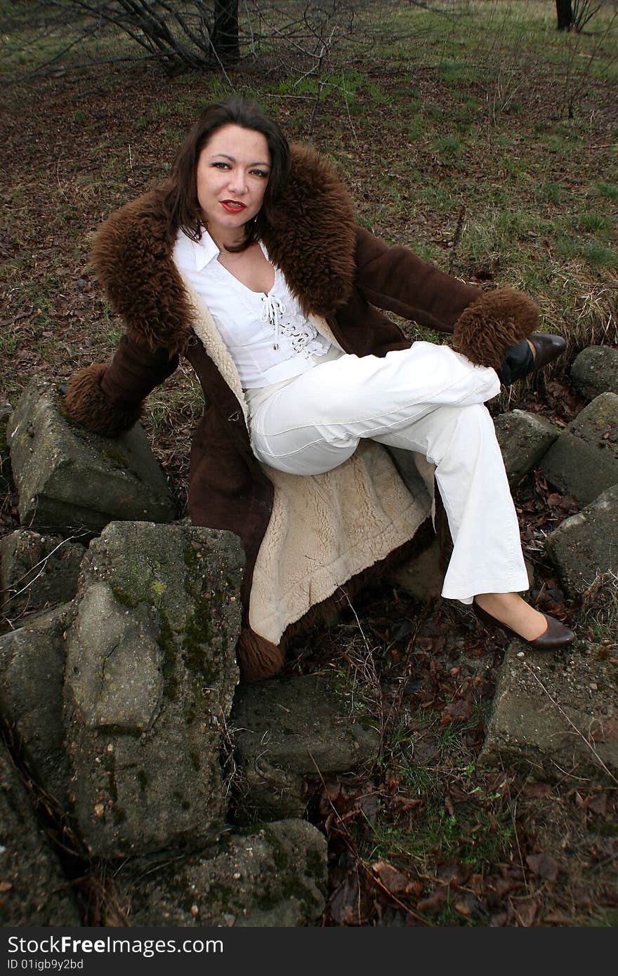 Smiling woman in sheepskin coat sitting on the rock.