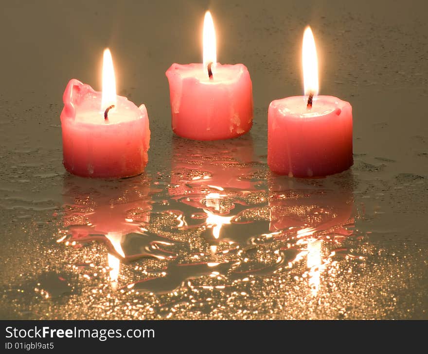 Candles, lit, standing on a wet surface that reflects light