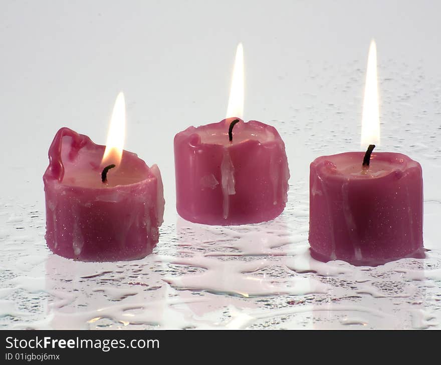 Candles, lit, standing on a wet surface that reflects light