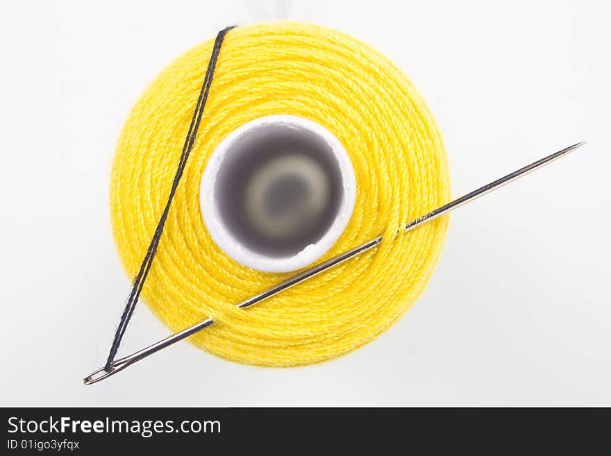 Close uyp of a yellow sewing spool with a needle