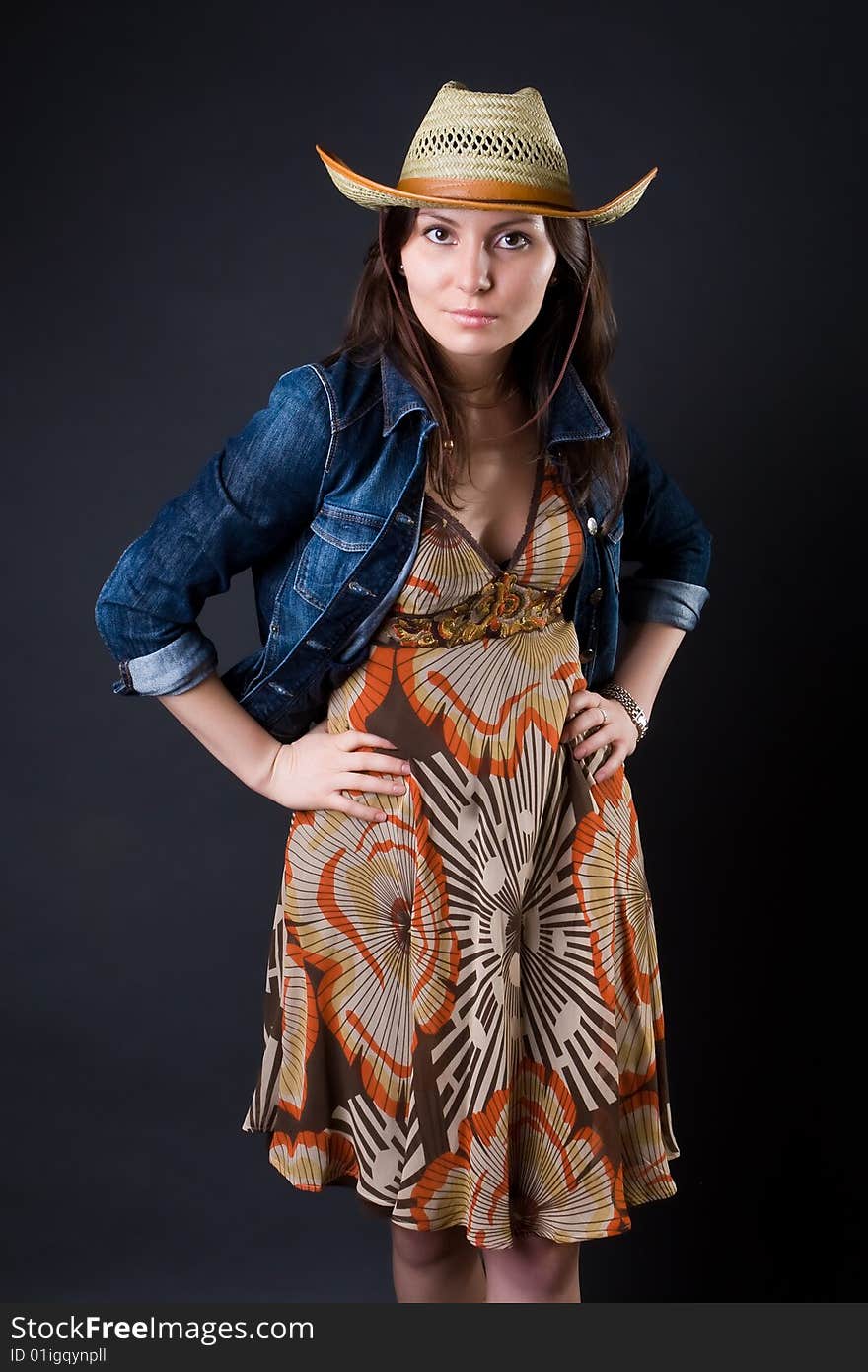 Girl in a cowboy's hat and a jeans jacket against a dark background. Girl in a cowboy's hat and a jeans jacket against a dark background