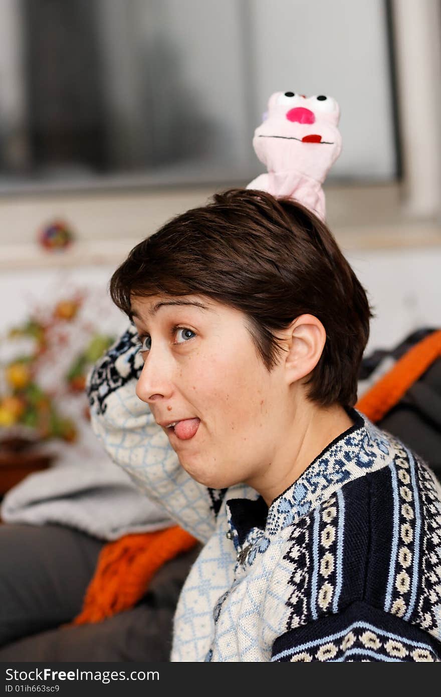 Young woman sticks out her tongue and has a doll on her head that sticks out her tongue too.