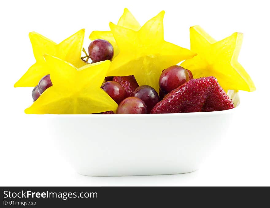 Colorful starfruit with strawberries and grapes in a white bowl isolated on white background with copy space