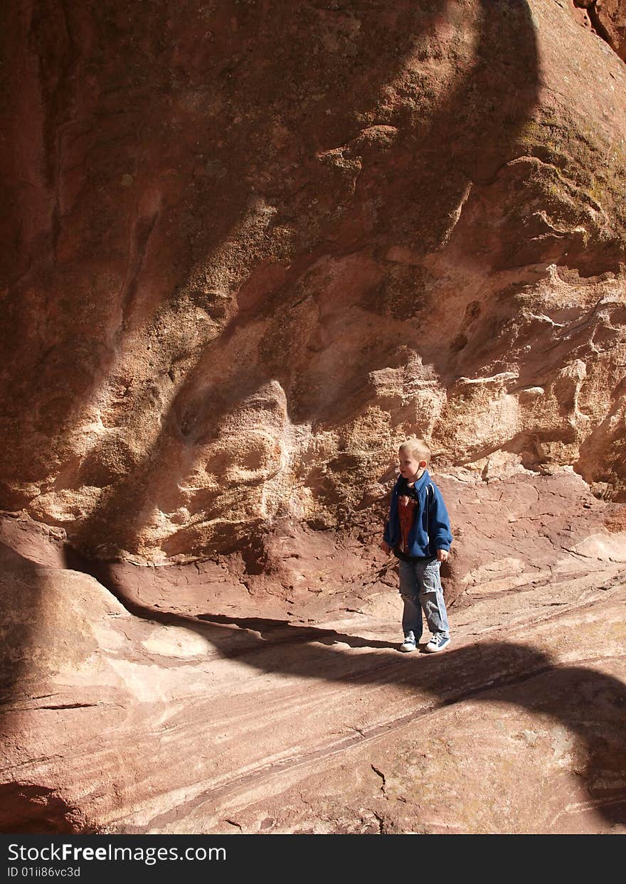 A color image of a young boy standing under a huge red rock cliff. A color image of a young boy standing under a huge red rock cliff.