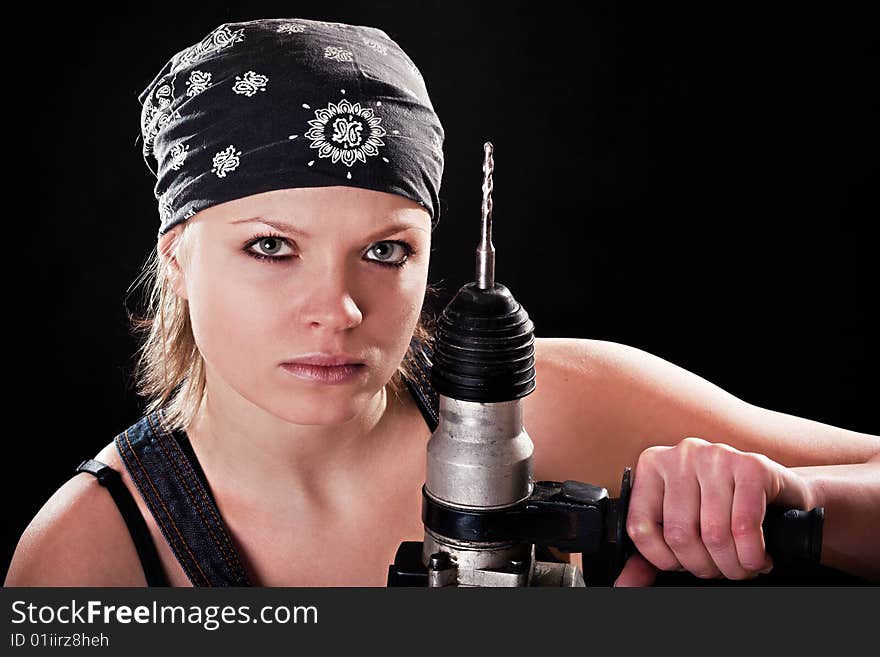 Severe young woman with a drill on black background