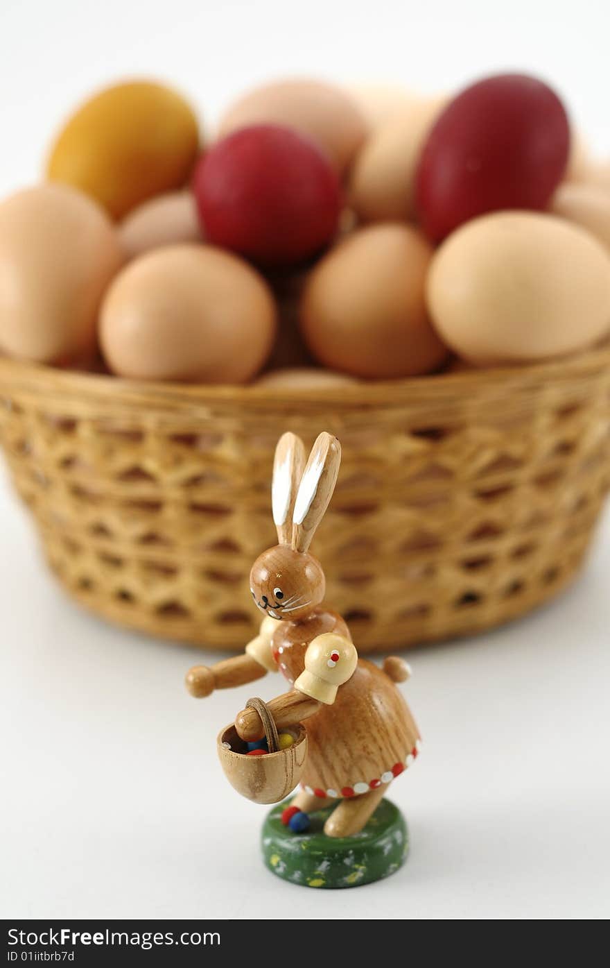 Wooden easter rabbit with basket and easter eggs in background, focus on rabbit