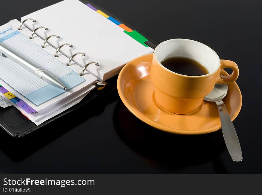 Orange coffee cup and a notepad on black background. Orange coffee cup and a notepad on black background