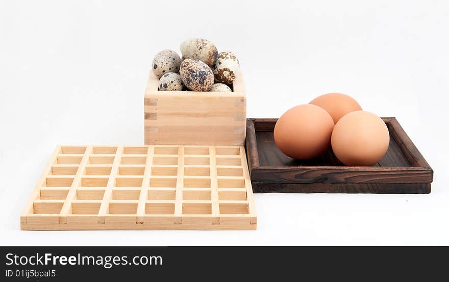 Zen inspired arrangement of quail and chicken eggs in wooden containers with square wooden grid on white background. Zen inspired arrangement of quail and chicken eggs in wooden containers with square wooden grid on white background