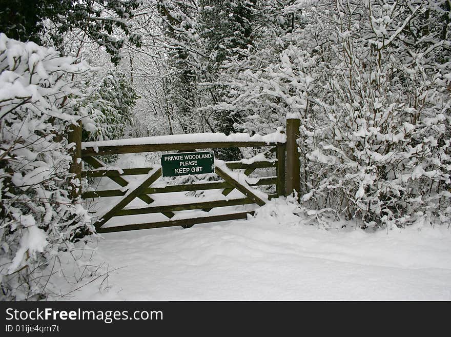 A keep out sign on a wooden gate that leads to a private woodland in winter