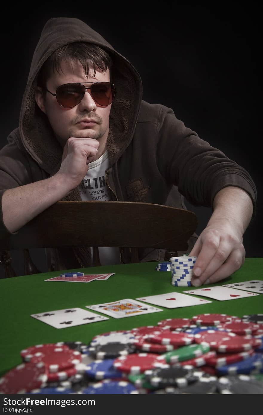 Man with sun glasses playing poker on green table. Chips and cards on the table. Man with sun glasses playing poker on green table. Chips and cards on the table.