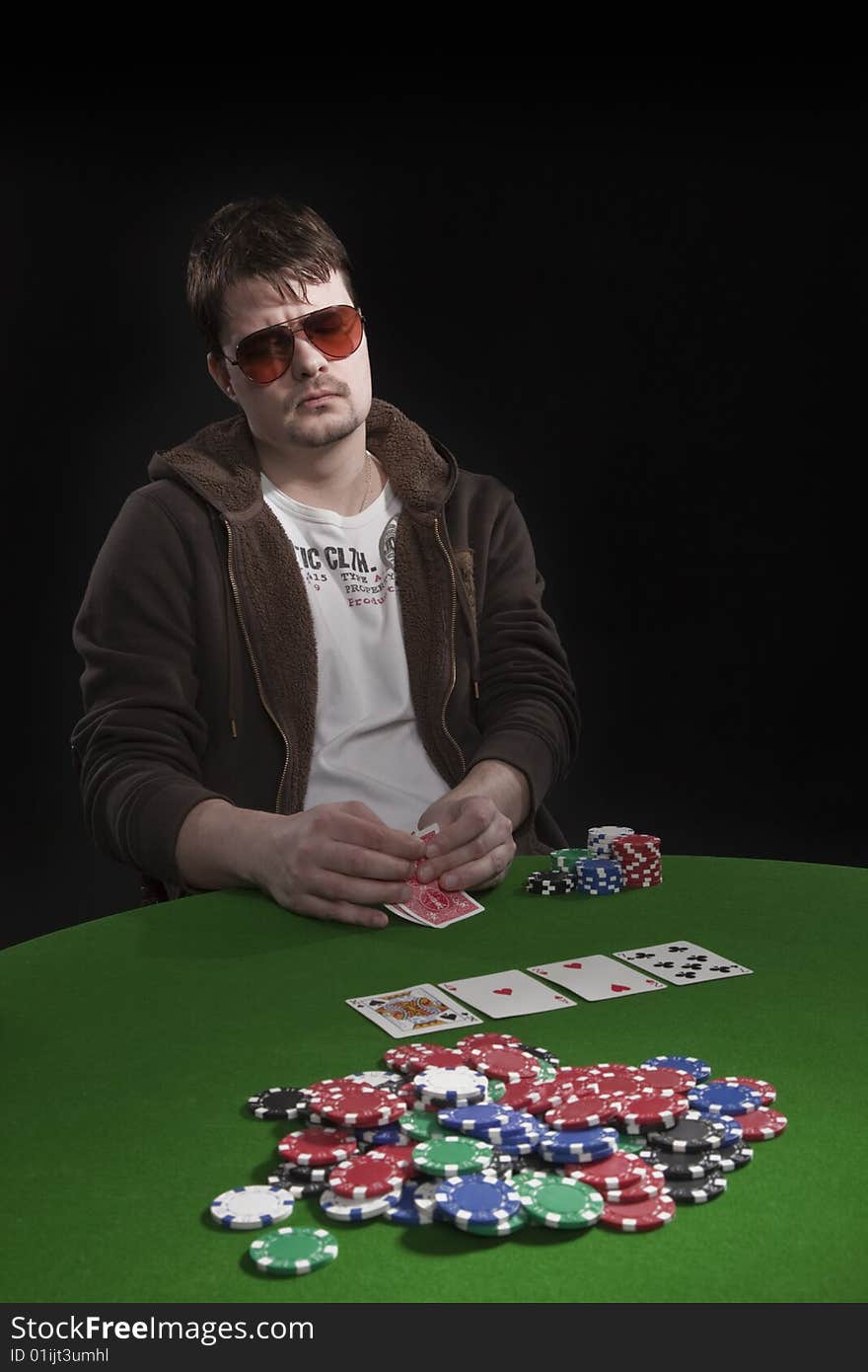 Man with sun glasses playing poker on green table. Chips and cards on the table. Man with sun glasses playing poker on green table. Chips and cards on the table.