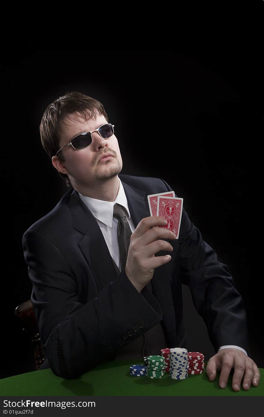 Man in suit with sun glasses playing poker on green table. Chips and cards on the table. Man in suit with sun glasses playing poker on green table. Chips and cards on the table.