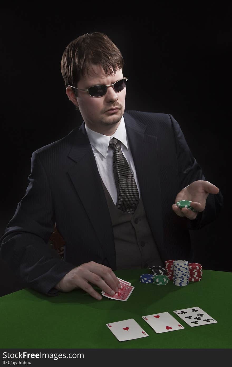 Man in suit with sun glasses playing poker on green table. Chips and cards on the table. Man in suit with sun glasses playing poker on green table. Chips and cards on the table.