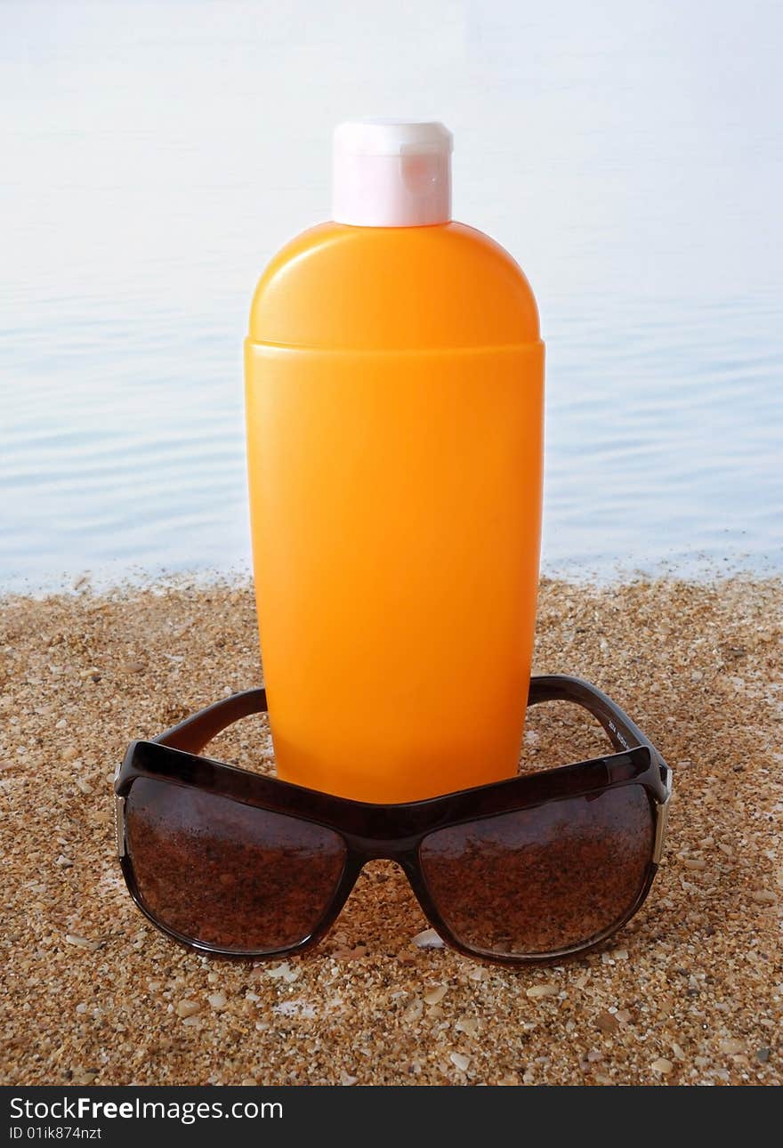 Antisun cream and antisun glasses on marine sand and on a background water