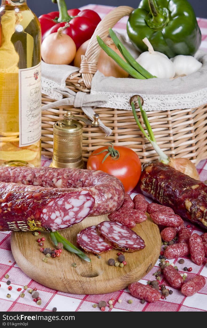 Salami sausage on a wooden plate with a background of a basket full of vegetables