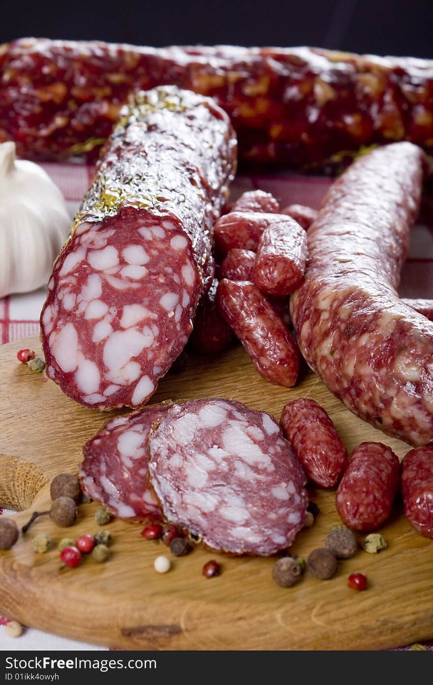 Salami sausage on a wooden plate with a background of a basket full of vegetables