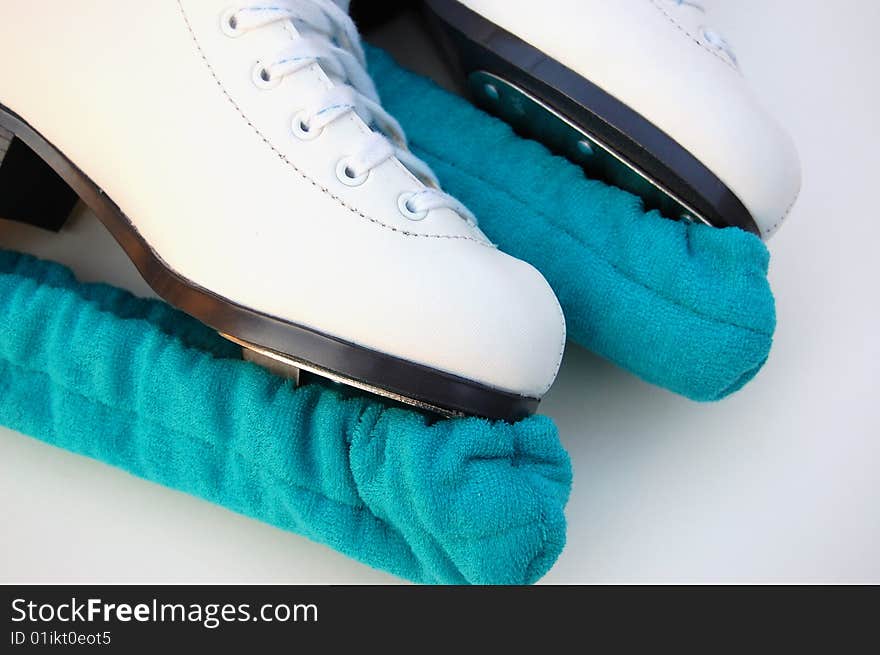 A pair of white ice figure skates with soakers on the blades. A pair of white ice figure skates with soakers on the blades