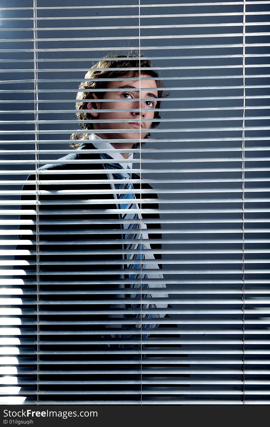 Young businessman behind a window blinds looking up. Young businessman behind a window blinds looking up