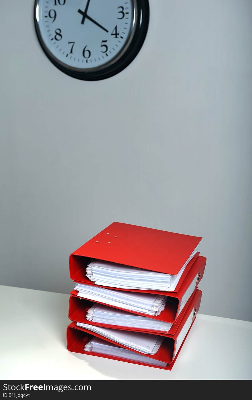 Stack of red folders on desk and a clock in background, deadline concept