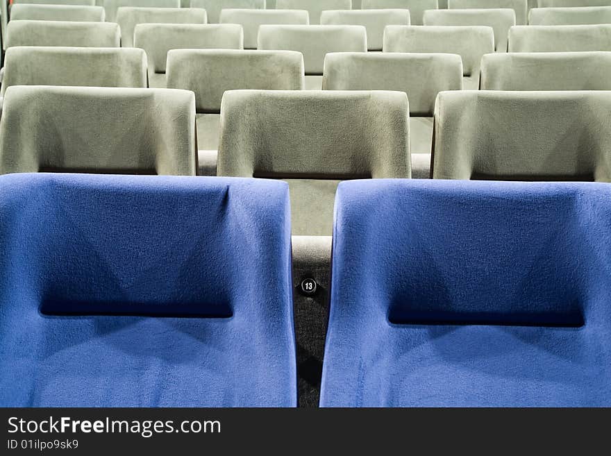 Seat number thirteen. Row of gray and blue chairs in auditorium. Seat number thirteen. Row of gray and blue chairs in auditorium.