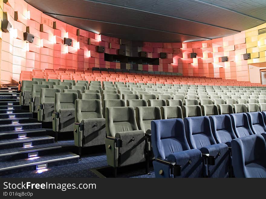 Empty new cinema auditorium with rows of blue, gray and red chairs and illuminated stairs. Empty new cinema auditorium with rows of blue, gray and red chairs and illuminated stairs.