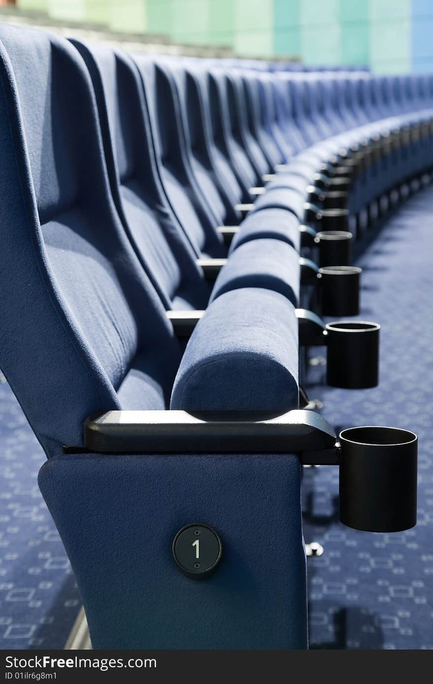 Row number one. Row of blue chairs in auditorium. Row number one. Row of blue chairs in auditorium.