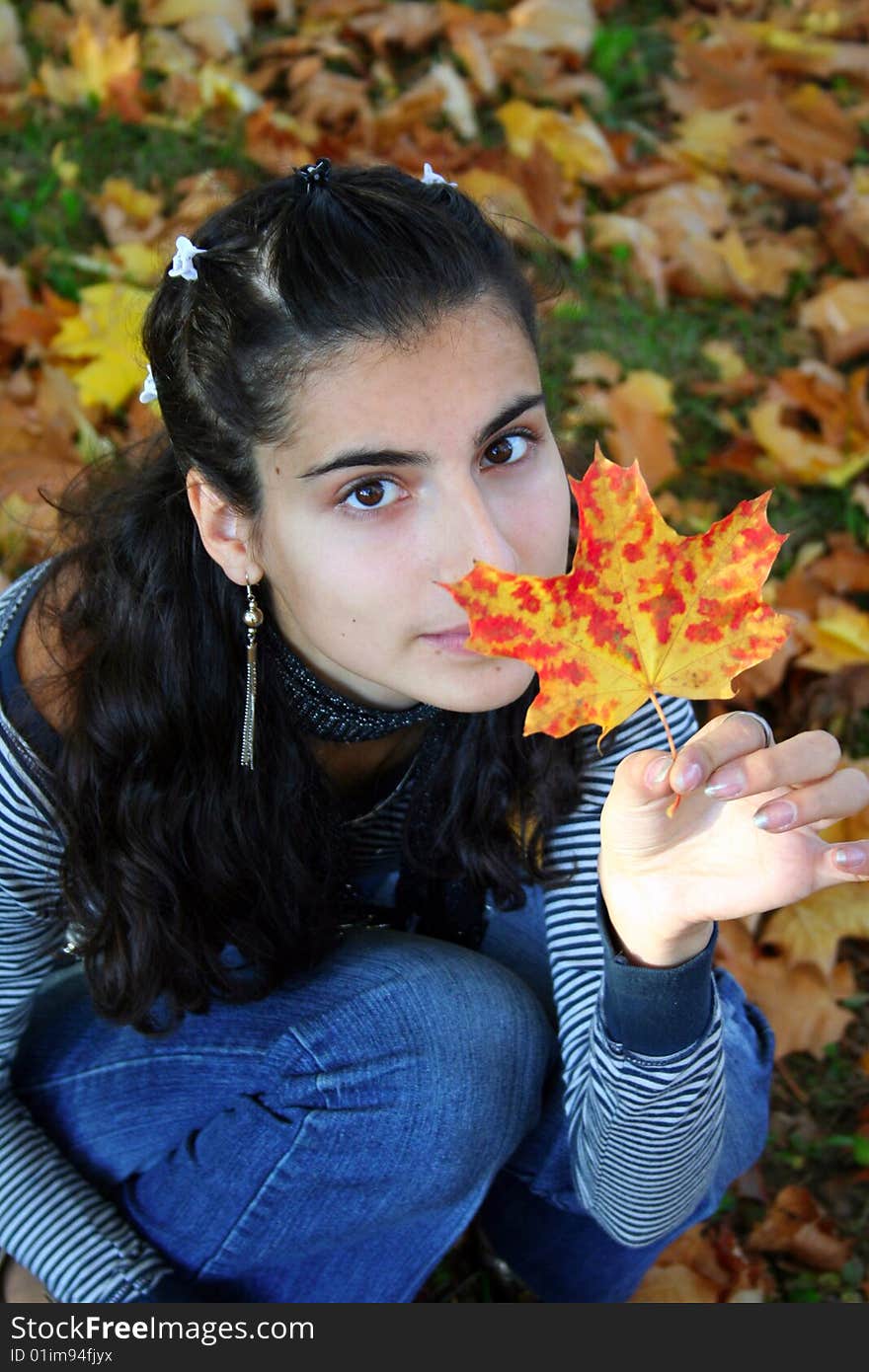 A girl sitting with the maple leaf in her hand. A girl sitting with the maple leaf in her hand