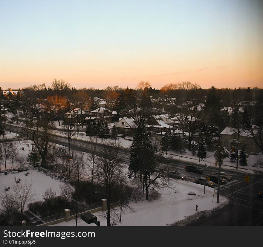 High angle shot on intersection at sunset with snow-covered roofs of houses and glowing trees. High angle shot on intersection at sunset with snow-covered roofs of houses and glowing trees.