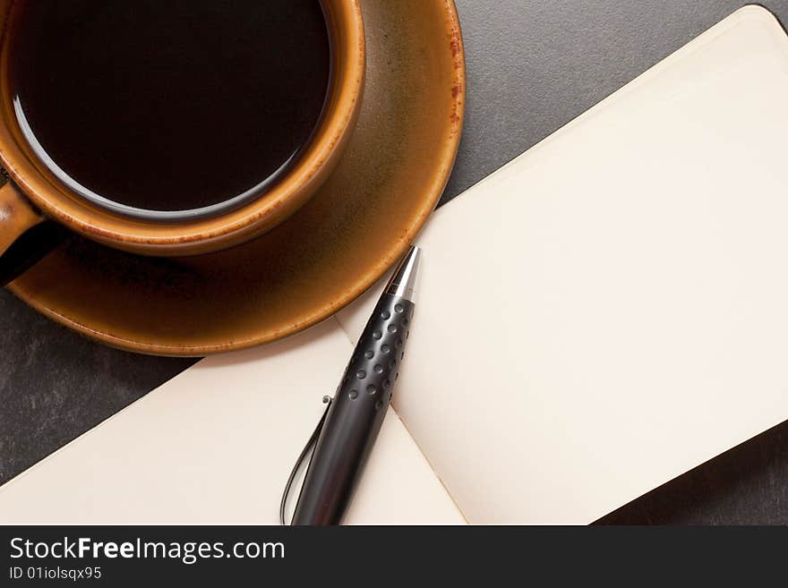 Hot cup of coffee with a blank notebook and pen ready to write down ideas. Hot cup of coffee with a blank notebook and pen ready to write down ideas