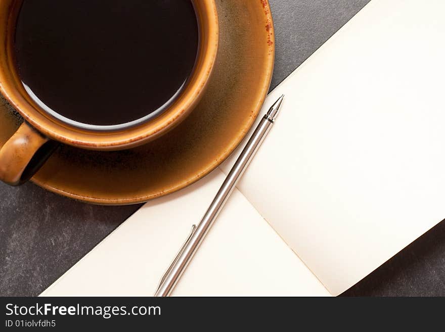 Hot cup of coffee with a blank notebook and pen ready to write down ideas. Hot cup of coffee with a blank notebook and pen ready to write down ideas