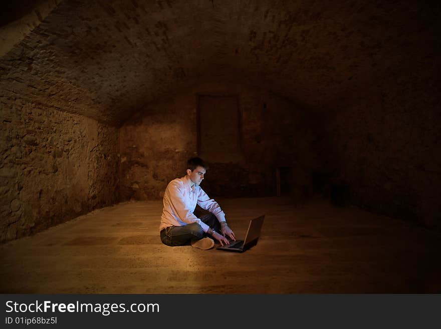 A man using a laptop in a cellar. A man using a laptop in a cellar