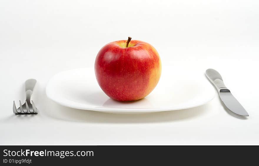 Fork, knife and red apple on white plate. Fork, knife and red apple on white plate