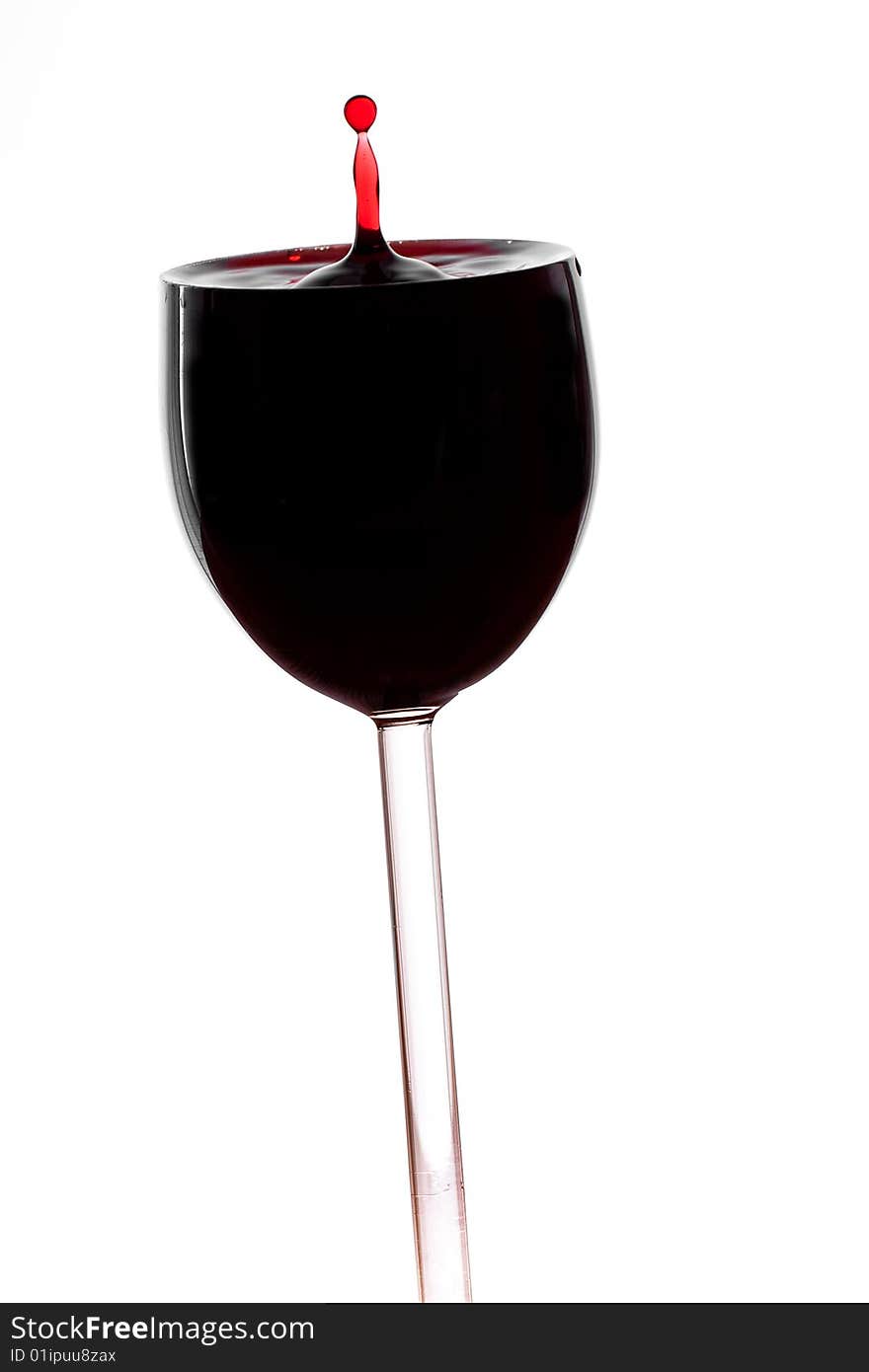 A drop of red wine falls into the glass isolated on white background