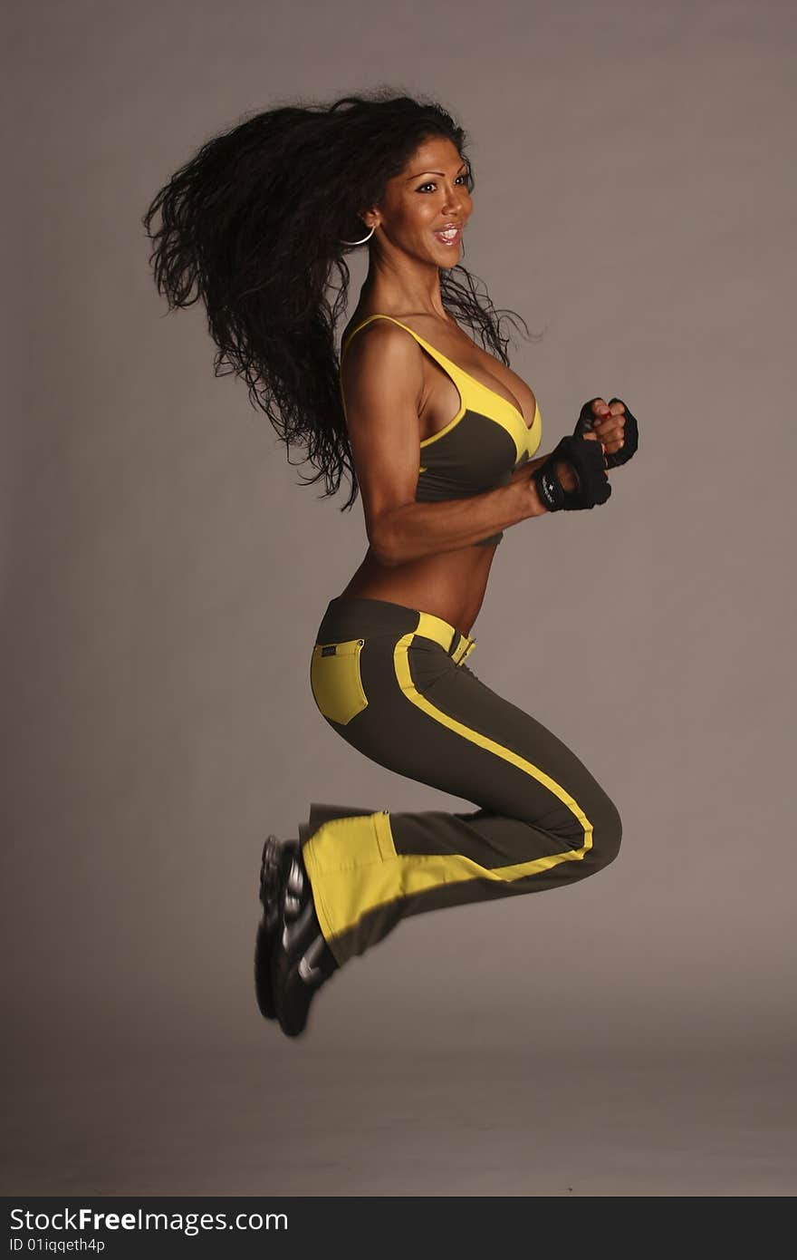 A fitness model with long flowing hair in studio wearing a green and yellow workout outfit with gloves and ear rings. A fitness model with long flowing hair in studio wearing a green and yellow workout outfit with gloves and ear rings.