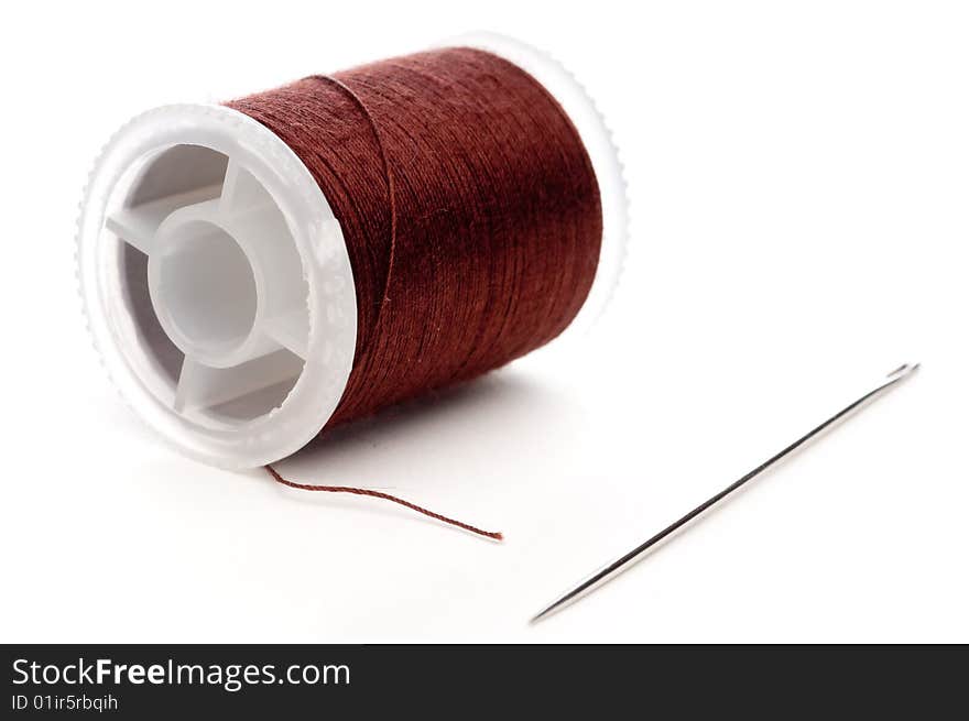 Closeup of a spool of brown thread and a needle