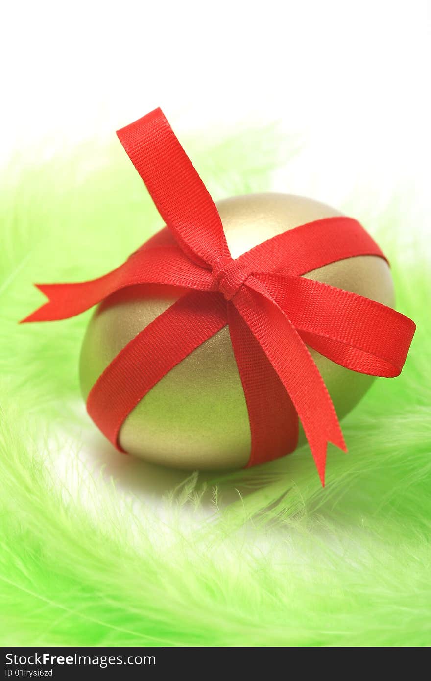 Golden egg wrapped around with red ribbon on green feathers.