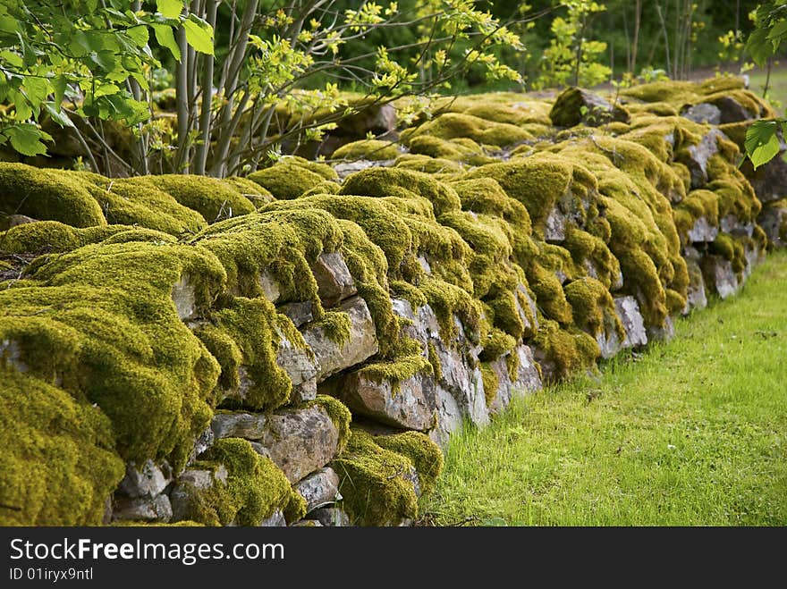 An old mossy stone wall near a chapel.