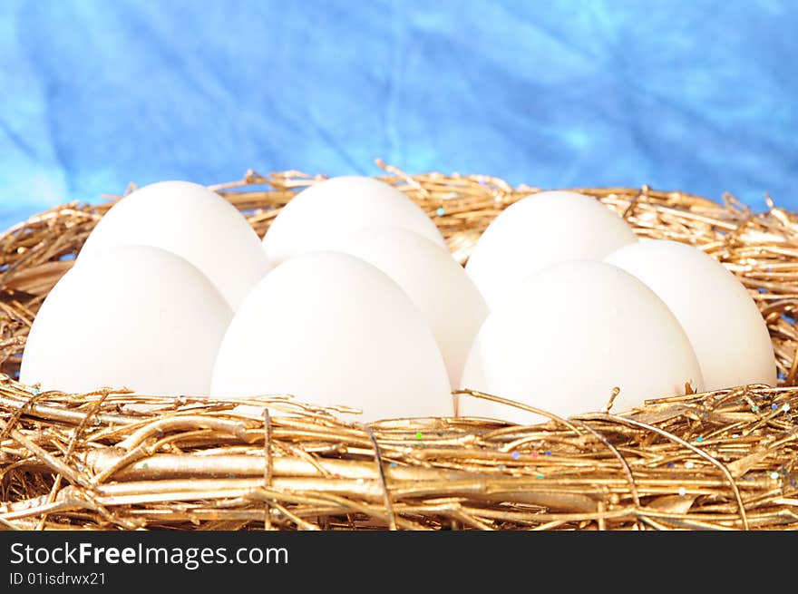 White eggs in golden nest on blue background