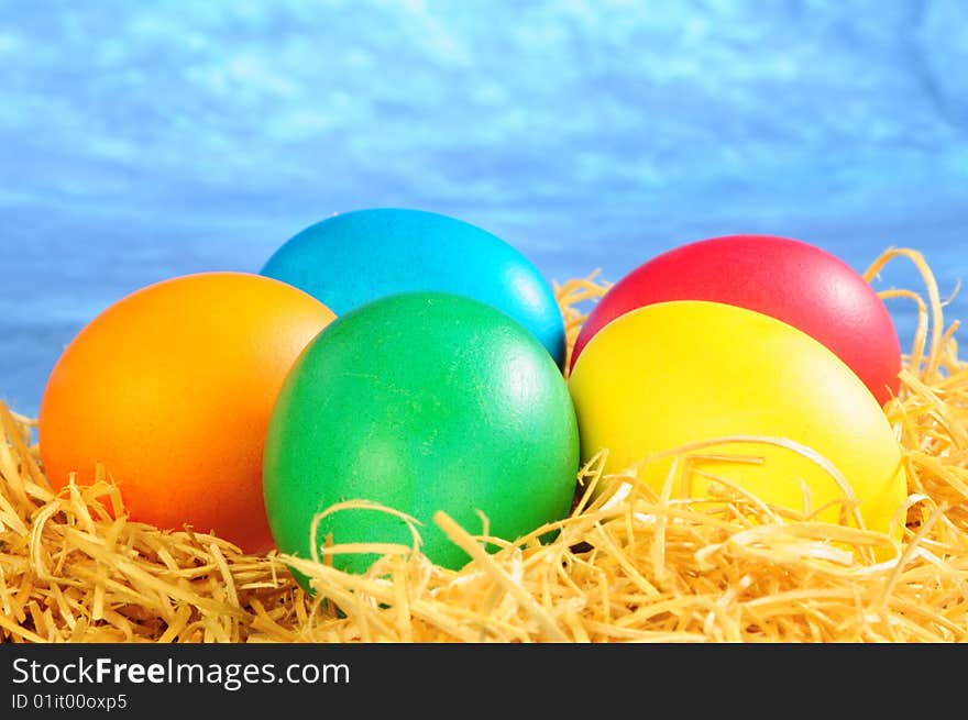 Five painted eggs on a straw on a blue background