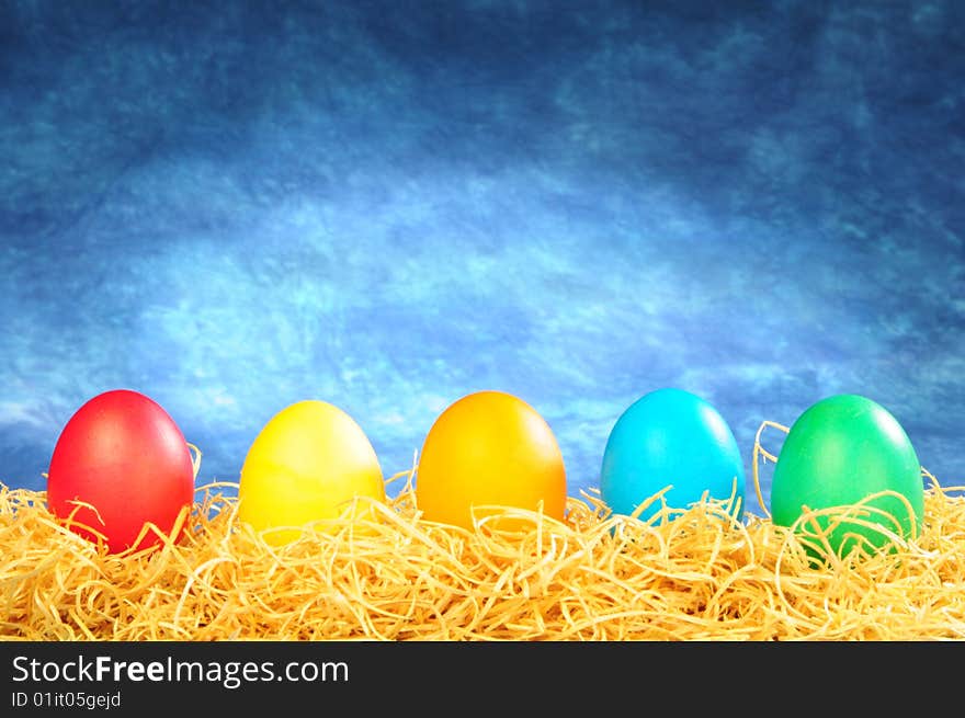 Five painted eggs on a straw on a blue background